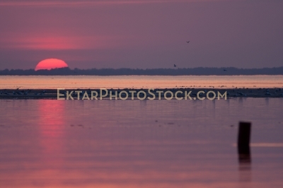 Red glowing sunset with sun and post in the water 